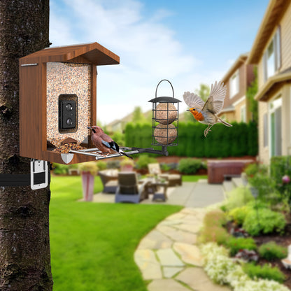Vogelhaus mit integrierter Kamera aus Holz an einem Baum befestigt, gefüllt mit Vogelfutter, mit ausziehbarer Sitzstange, hängendem Meisenknödelhalter und zwei Vögeln vor unscharfem Gartenhintergrund